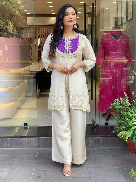 Elevate your ethnic style with this elegant cream kurti set featuring intricate embroidery and a striking purple yoke. Paired with flared pants, this outfit blends tradition with modern flair—perfect for festive occasions or graceful daywear.