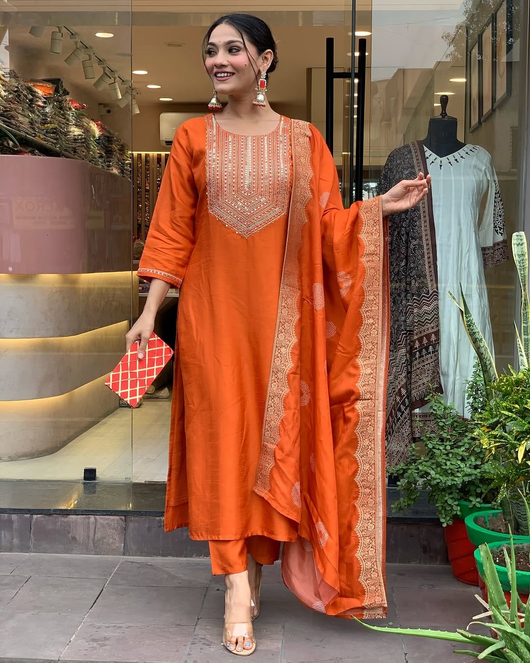 This vibrant orange kurti set exudes elegance with intricate embroidery and a luxurious dupatta featuring delicate border detailing